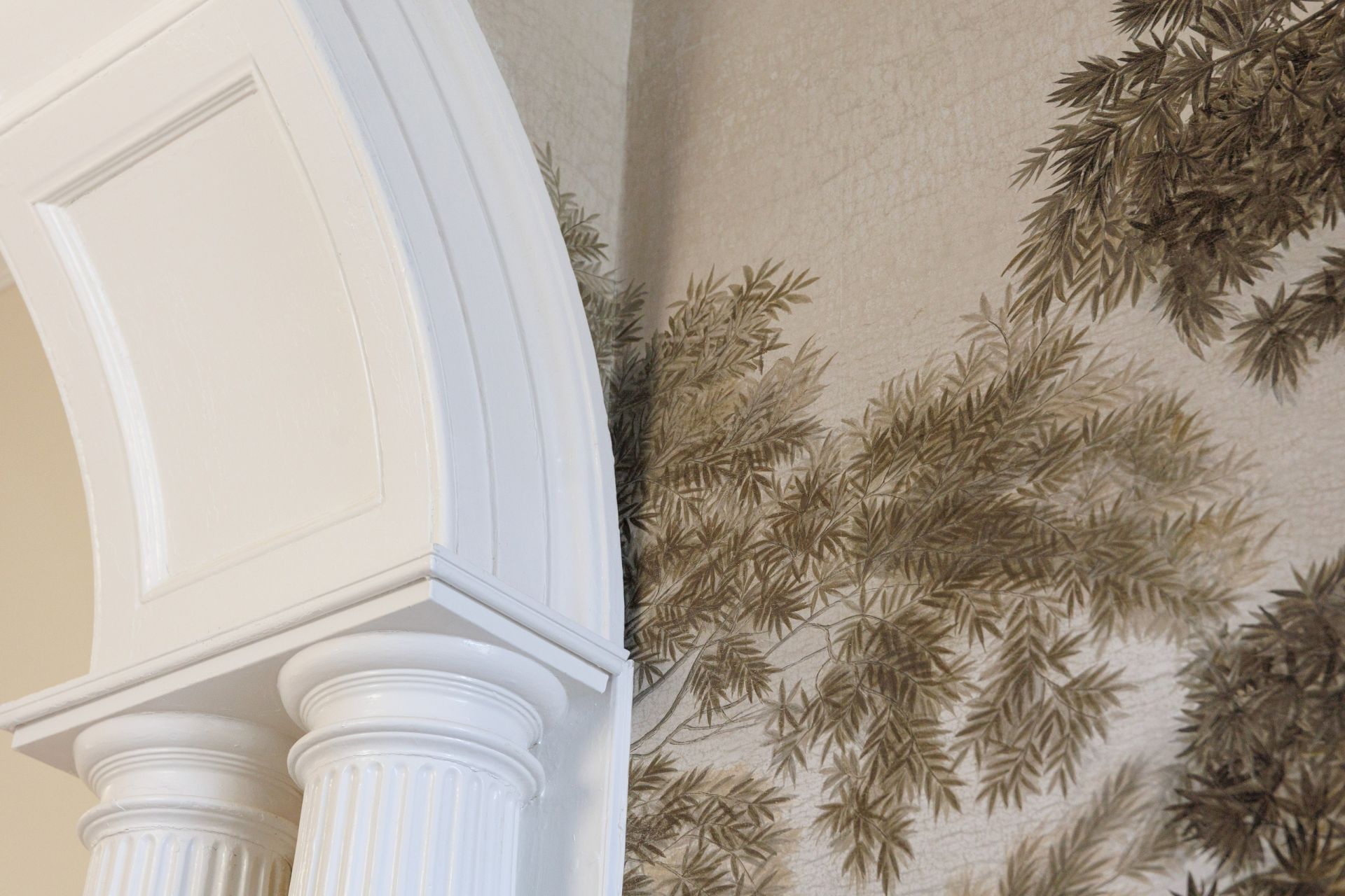 A white door frame and radiator sit beside tan wallpaper covered in green palm-leaf patterns in a room corner.