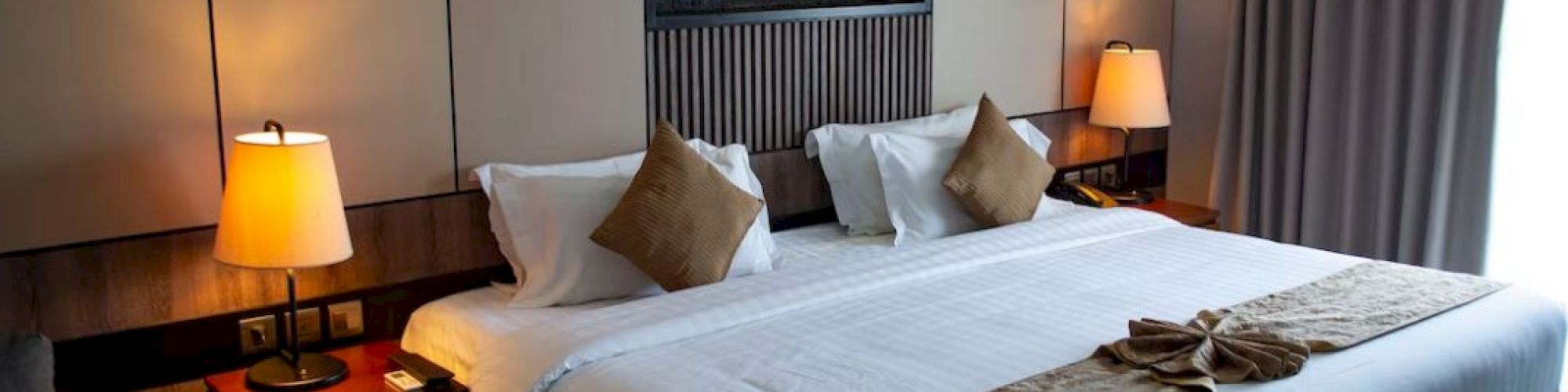 A neatly arranged hotel room with a king-size bed, bedside tables with lamps, and a modern wall decor above the headboard.