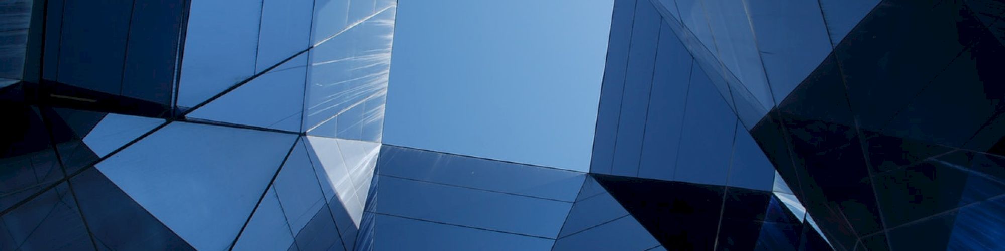 Abstract view of a modern glass building, looking upward at a clear sky through geometric, reflective surfaces.