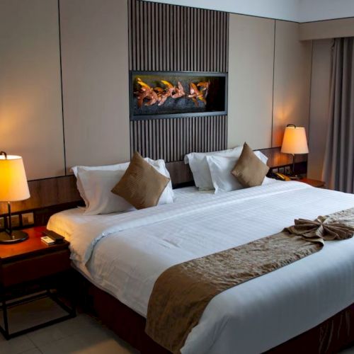 A neatly arranged hotel room with a large bed, lamps, decorative pillows, and a wall art piece above the bed.