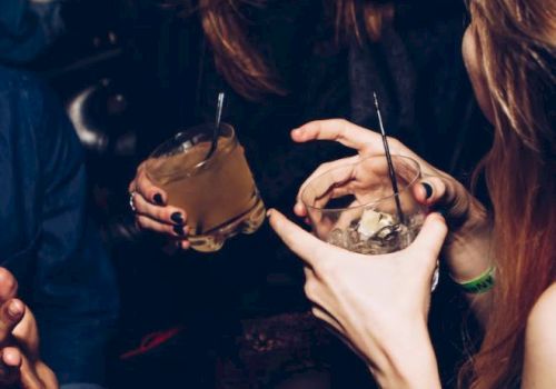 People are enjoying drinks in a lively setting, sharing laughter and conversation, with dim lighting creating a cozy atmosphere.