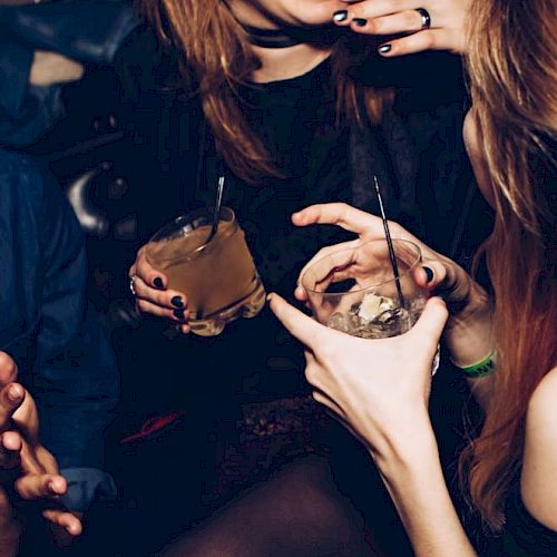 People are enjoying drinks in a lively setting, sharing laughter and conversation, with dim lighting creating a cozy atmosphere.