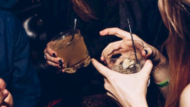 People are enjoying drinks in a lively setting, sharing laughter and conversation, with dim lighting creating a cozy atmosphere.
