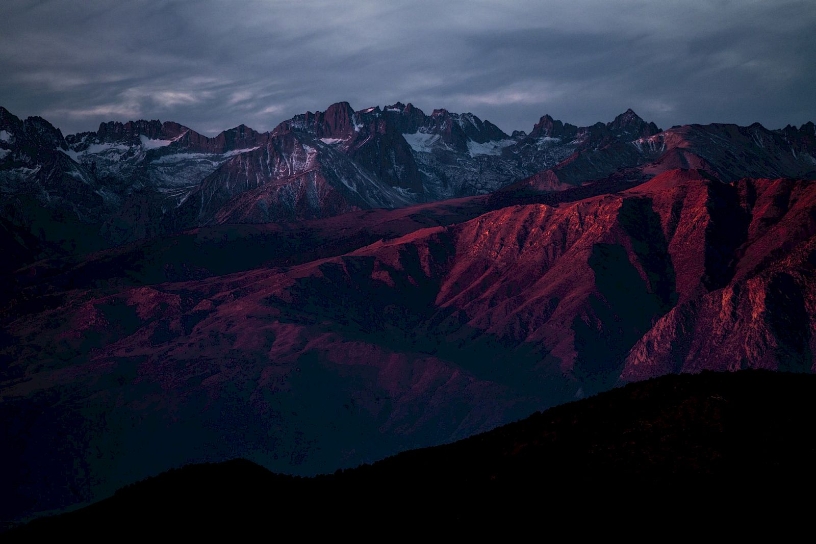 A mountain range under a dramatic sky with a reddish tint on the peaks, creating a striking natural landscape.