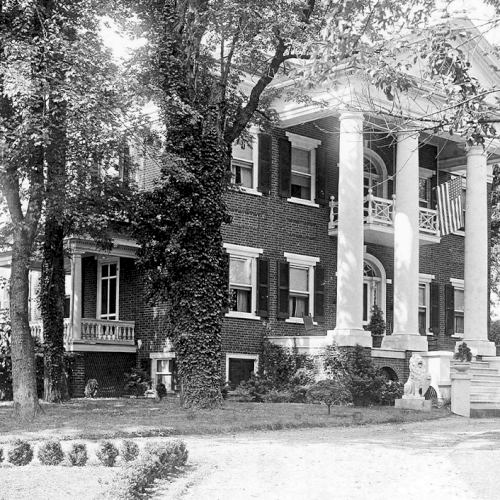 A large, historic brick house with tall columns, surrounded by trees and a manicured lawn, is featured in the image.