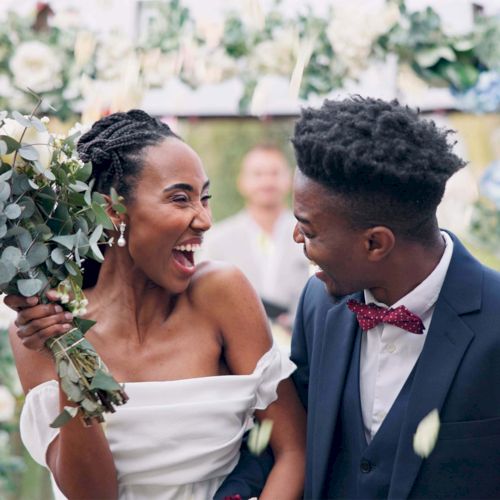 A joyful couple celebrates their wedding, holding a bouquet in front of an arch adorned with flowers and greenery.