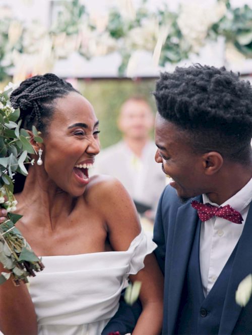A joyful couple celebrates their wedding, holding a bouquet in front of an arch adorned with flowers and greenery.