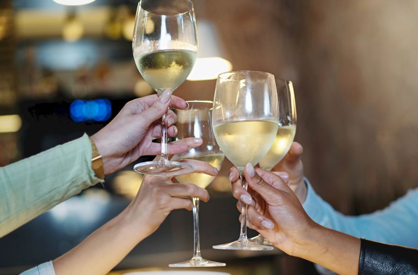 A group of hands holding and clinking glasses of white wine in a celebratory toast.