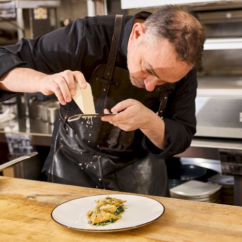 A chef is carefully grating cheese onto a dish in a professional kitchen, focused on presentation.