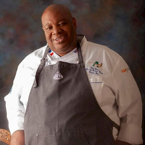 The image shows a person wearing a chef's coat and apron, posing and smiling, with a colorful backdrop behind.