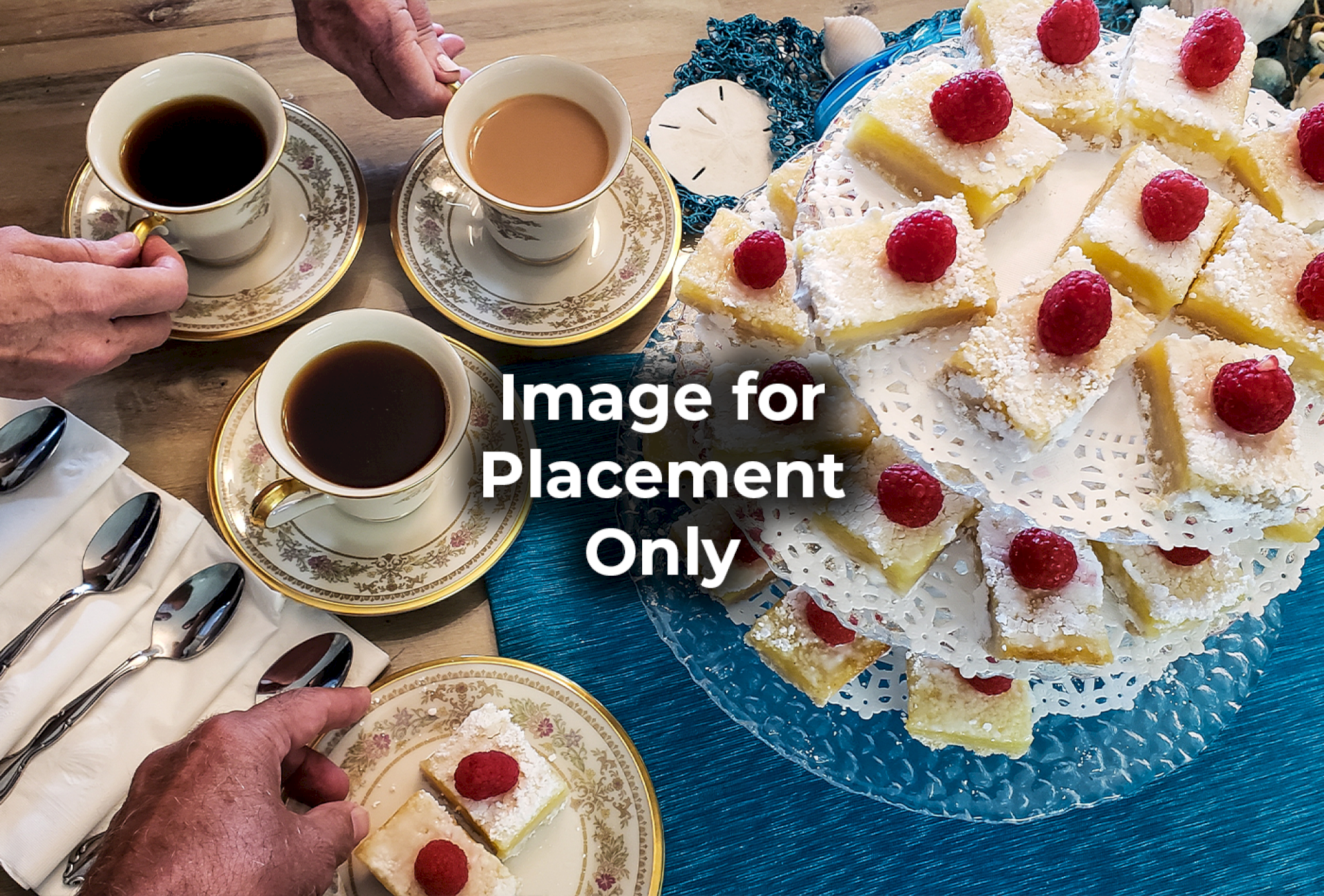 A table with cups of coffee, tea, and a two-tiered tray of raspberry-topped desserts is shown. Spoons are nearby on a napkin.