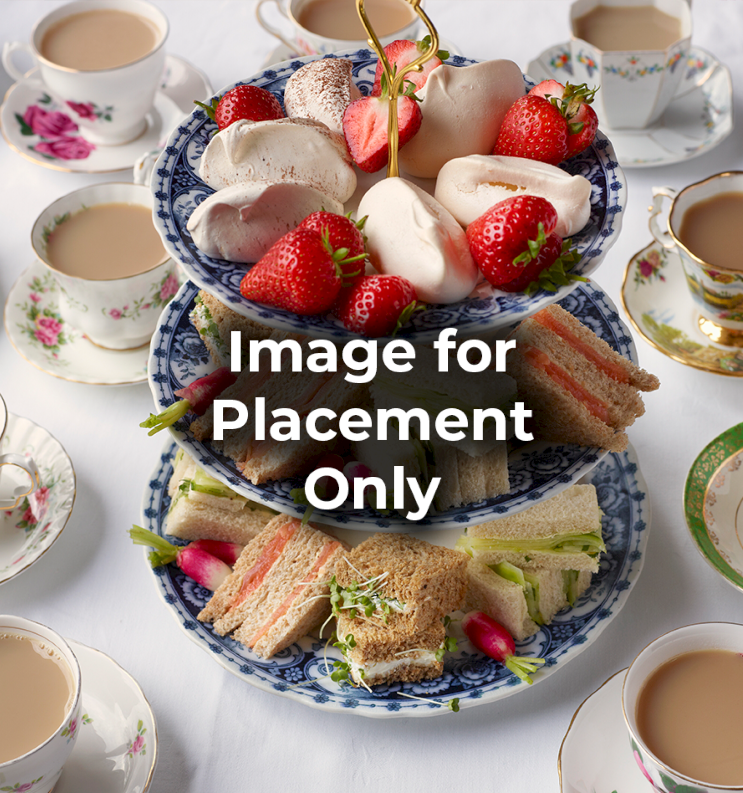 A tiered tray with strawberries, pastries, and sandwiches, surrounded by tea cups on a elegantly set table for tea time.