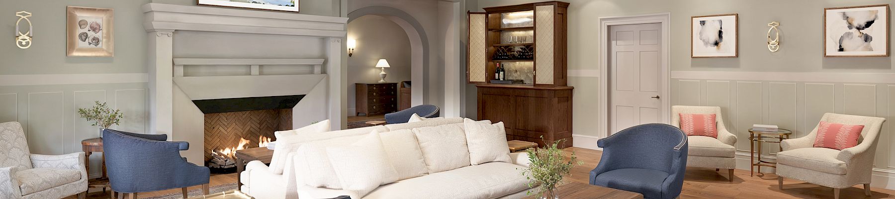 This image shows a cozy living room with a beamed ceiling, elegant furniture, chandeliers, and artwork on the walls.