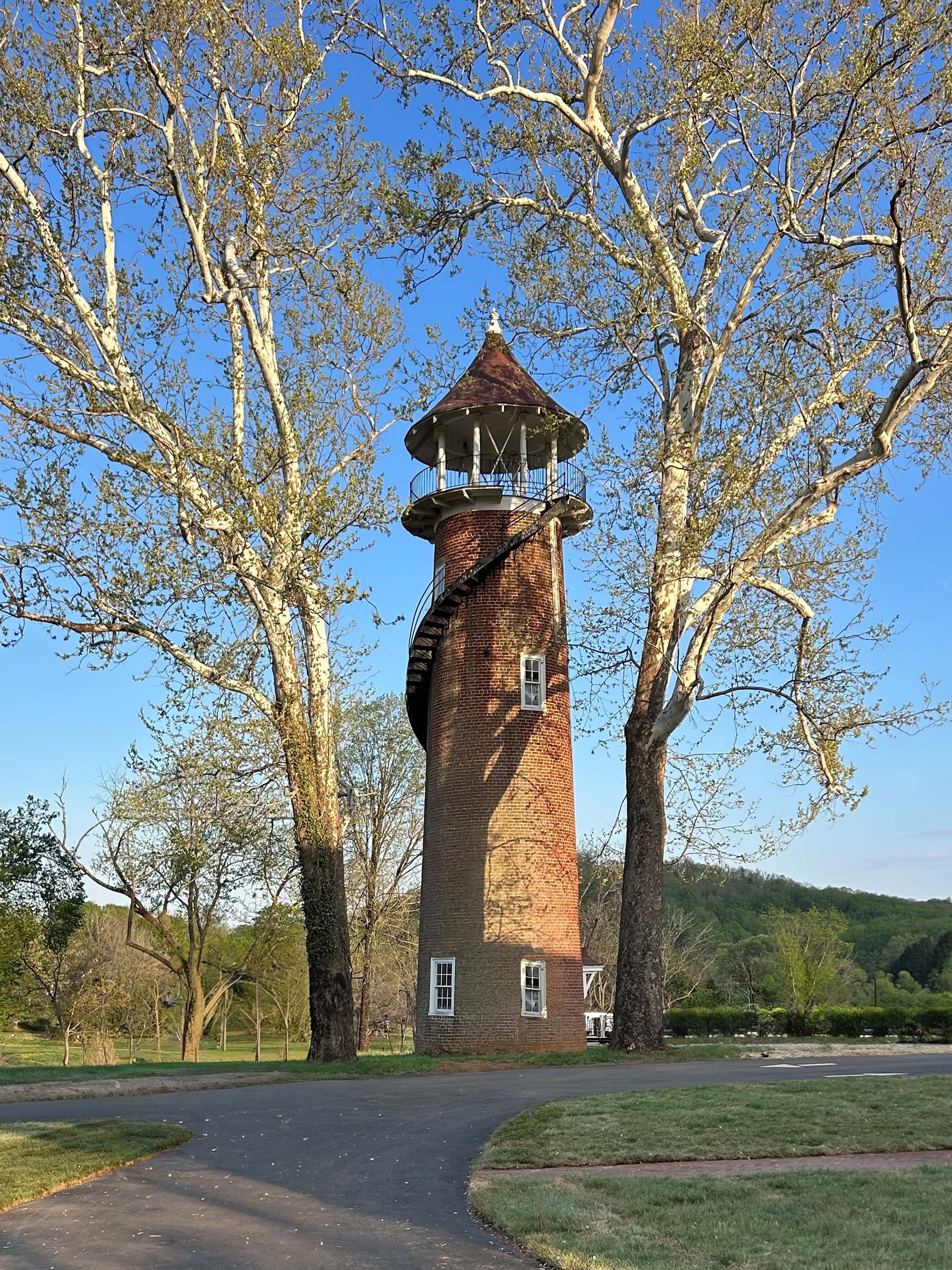 A brick spiral observation tower with a conical roof, windows, surrounded by leafless trees and a clear blue sky.