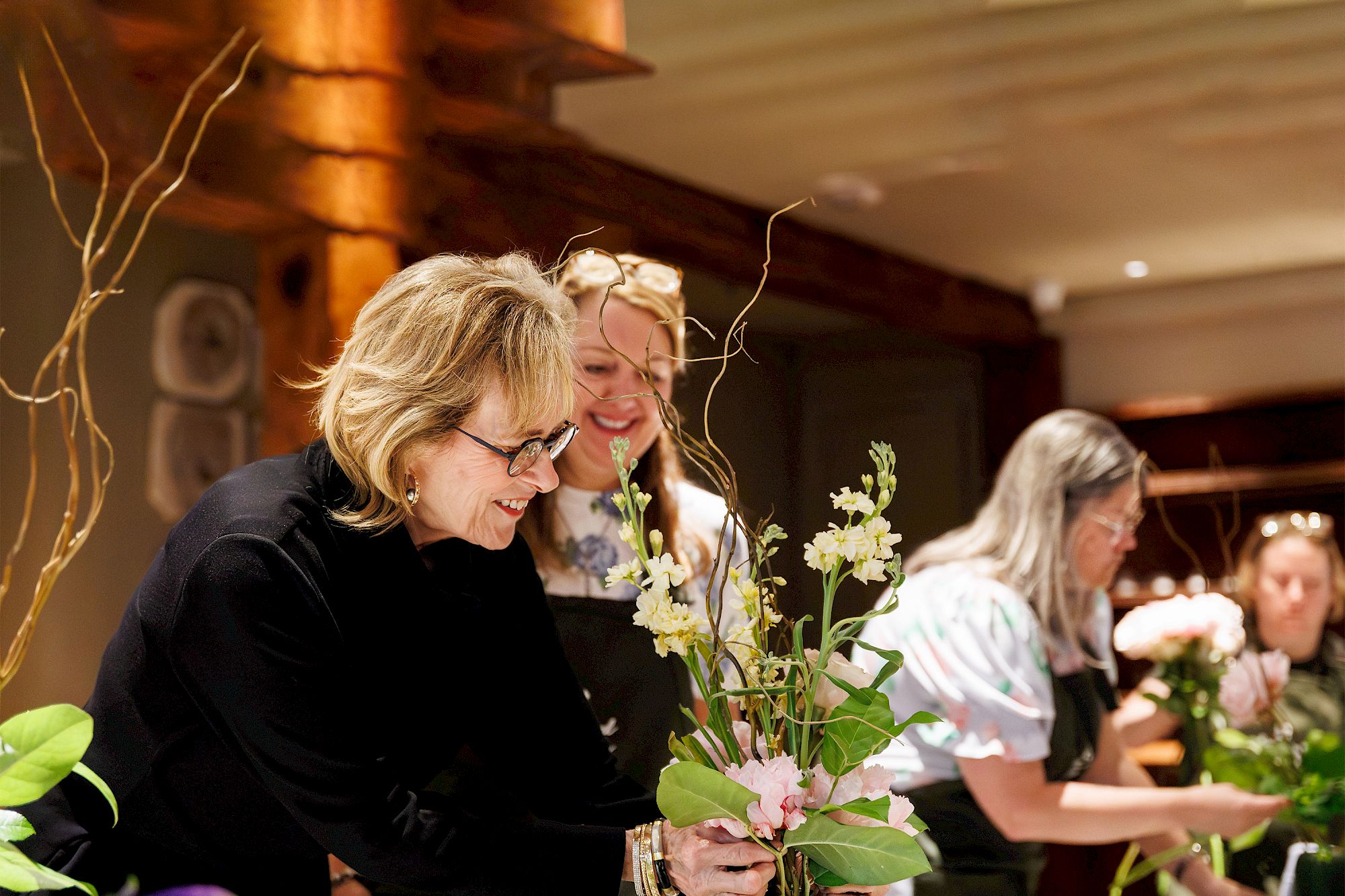 People arranging flowers at a workshop, focusing on stems and greenery in a cozy indoor space.