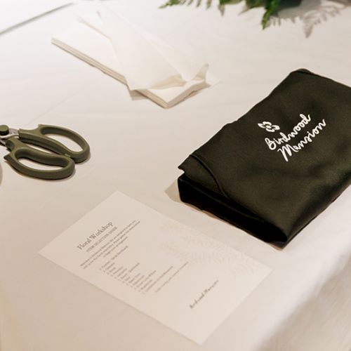 A white table with a black fabric pouch labeled &ldquo;Bridal Handbook,&rdquo; a pair of scissors, a card, and some paper on display.