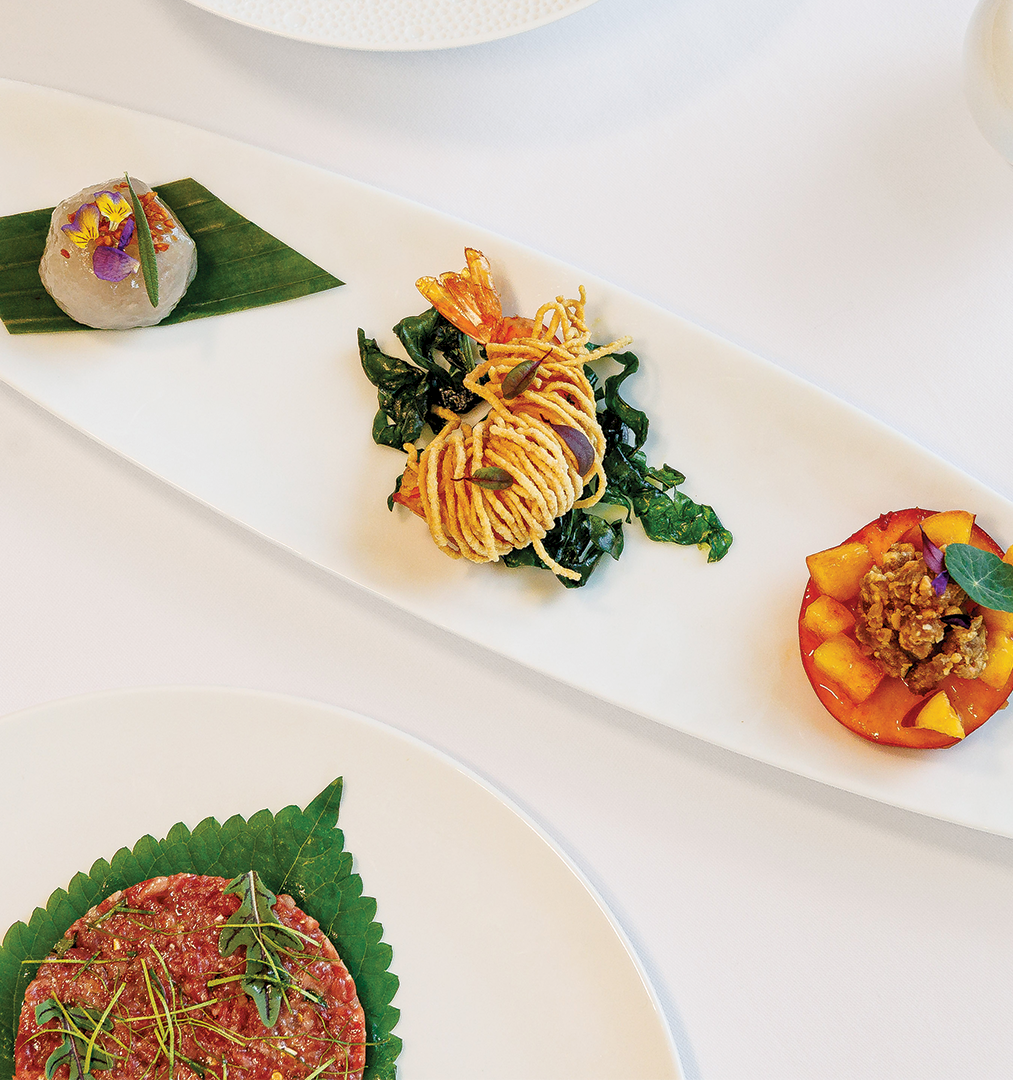 Gourmet dishes plated on white porcelain, featuring seafood and greens with colorful garnishes and sauces, ready to serve.