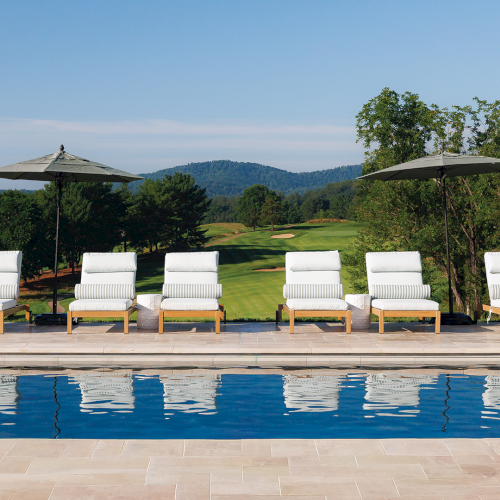 White cushioned lounge chairs sit by the swimming pool with umbrellas, overlooking the lush green Birdwood golf course and distant hills.