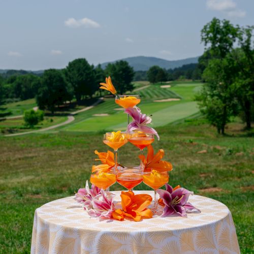 A floral drink display&mdash;orange and pink lilies atop glasses of bright cocktails on a table, with rolling hills behind it.