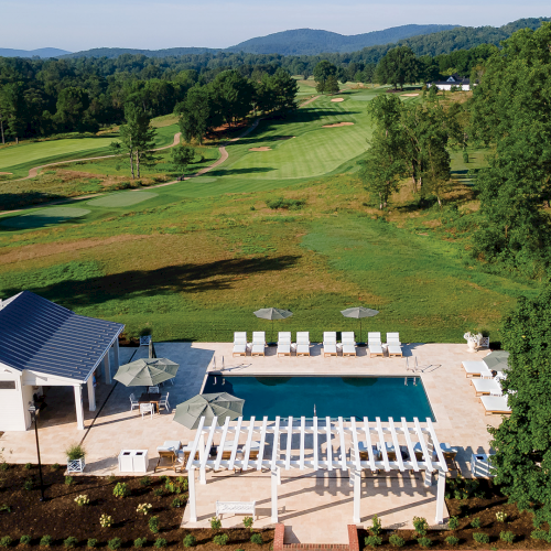 Aerial view of a hillside golf course with a home, swimming pool, and patio by the fairway at golden hour.