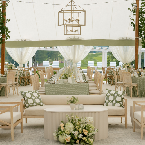 An elegant outdoor wedding reception inside a white tent, with chandeliers, rows of chairs, and lush floral decor.