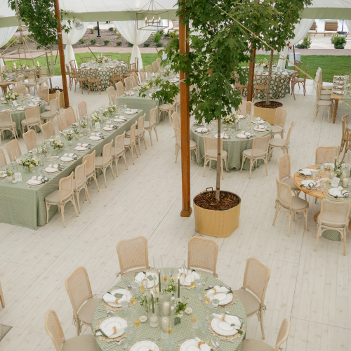 An elegant outdoor wedding reception setup with round tables, floral centerpieces, and string lights under a large white tent, inviting and festive.