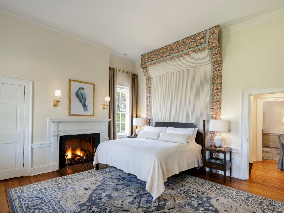 A bright bedroom with a cozy bed, burning fireplace, patterned curtains, framed bird artwork, and elegant classic decor.