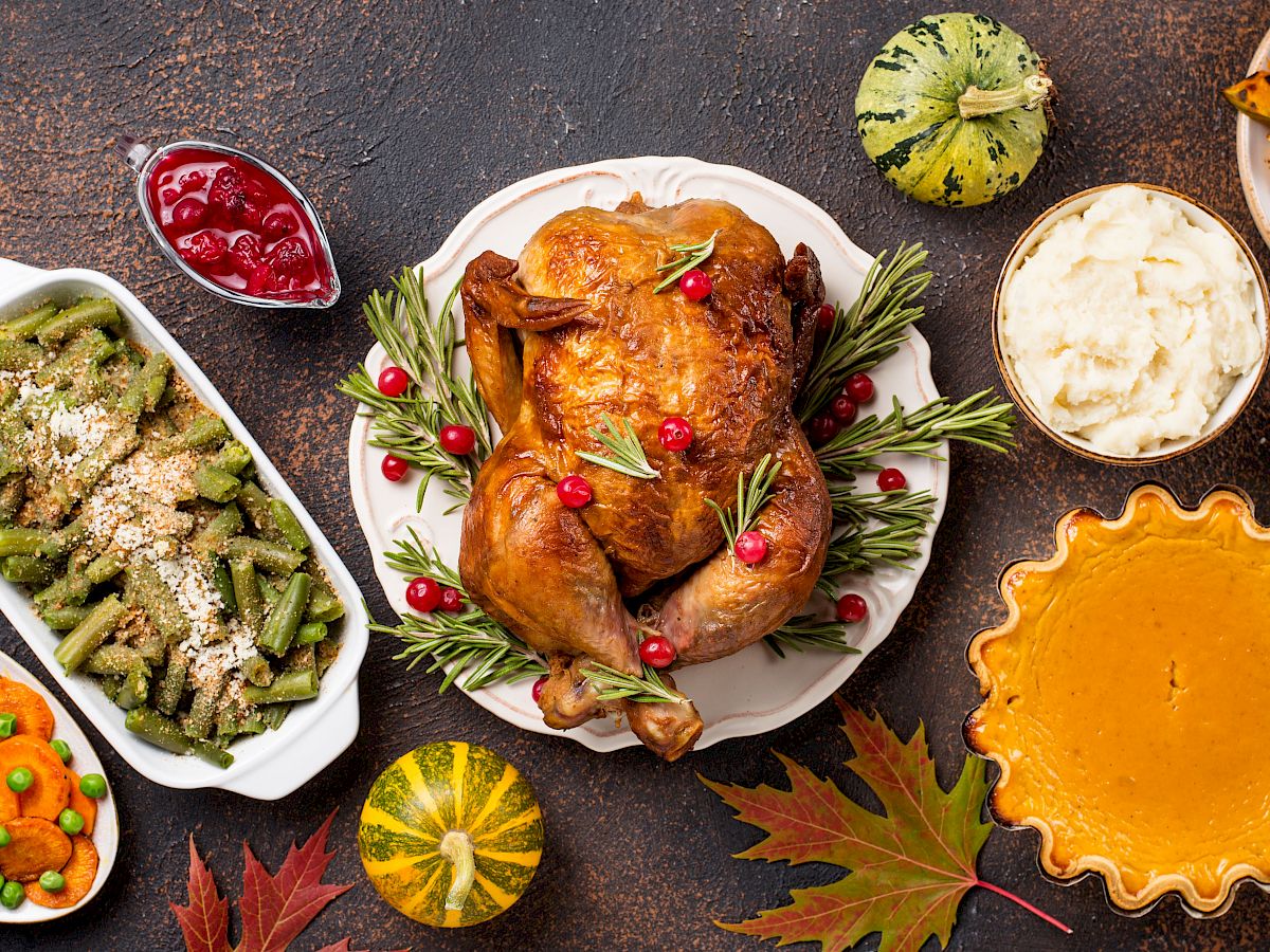 Roasted turkey with rosemary, plus cranberry sauce, green beans, mashed potatoes, squash, and corn on a rustic table.