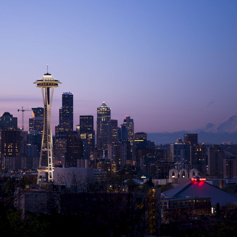 Seattle skyline at twilight featuring the Space Needle, with Mount Rainier in the background against a clear sky.