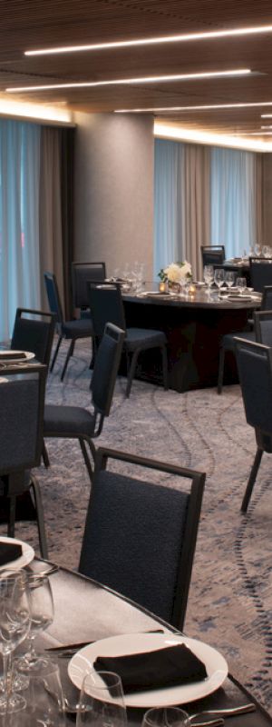 A banquet hall with round tables set for an event, featuring elegant tableware, black napkins, and floral centerpieces.