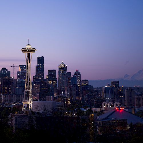Seattle skyline at dusk featuring the Space Needle and Mount Rainier in the background, with a purple and blue sky enhancing the scene.