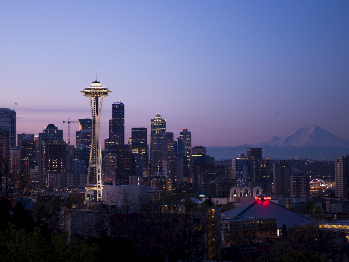Seattle skyline at dusk featuring the Space Needle and buildings, with Mount Rainier in the background under a clear sky.