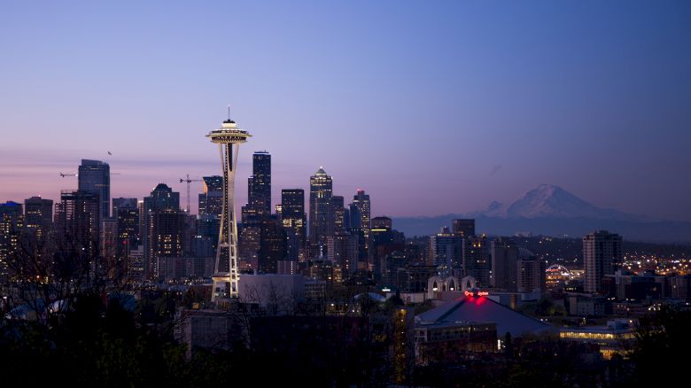 Seattle skyline at dusk featuring the Space Needle and buildings, with Mount Rainier in the background under a clear sky.